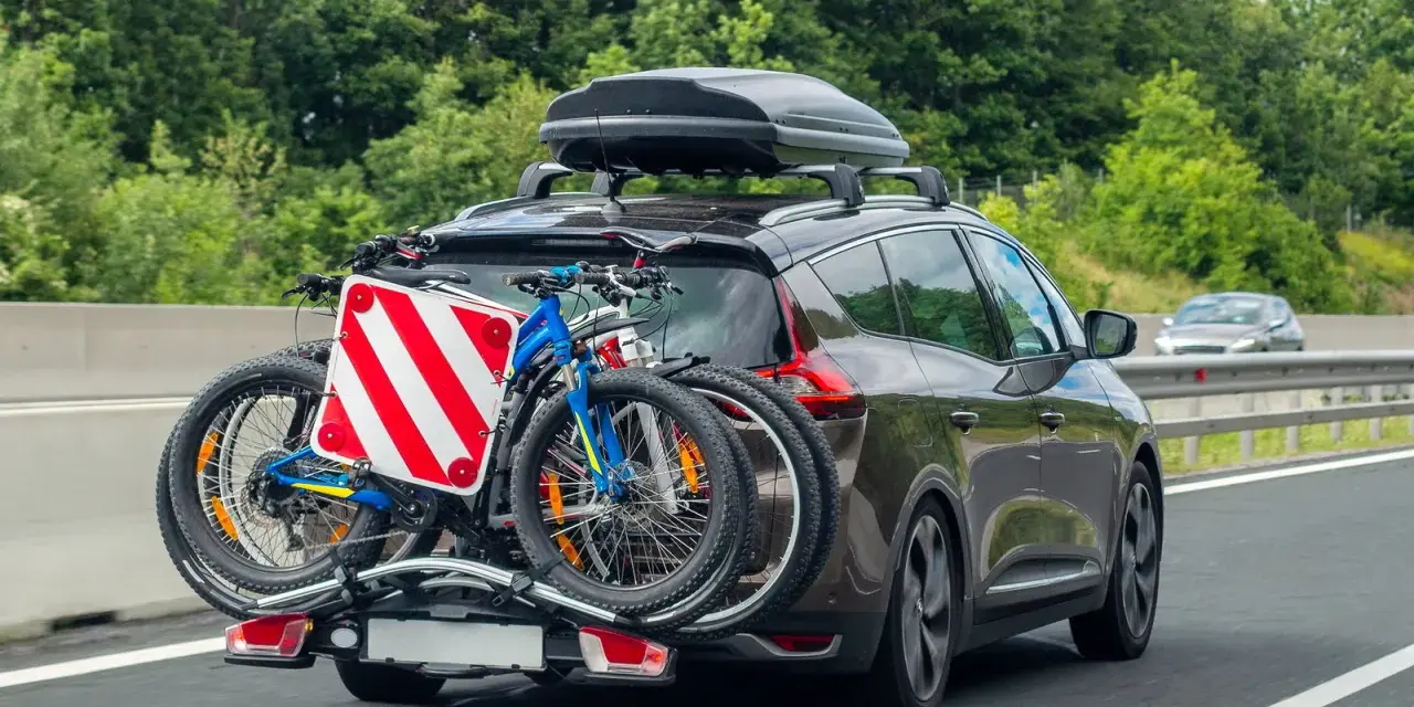 Auto in autostrada con due biciclette sul retro e box sul tetto. Il carico sporgente è ben visibile, pronto per un'avventura.