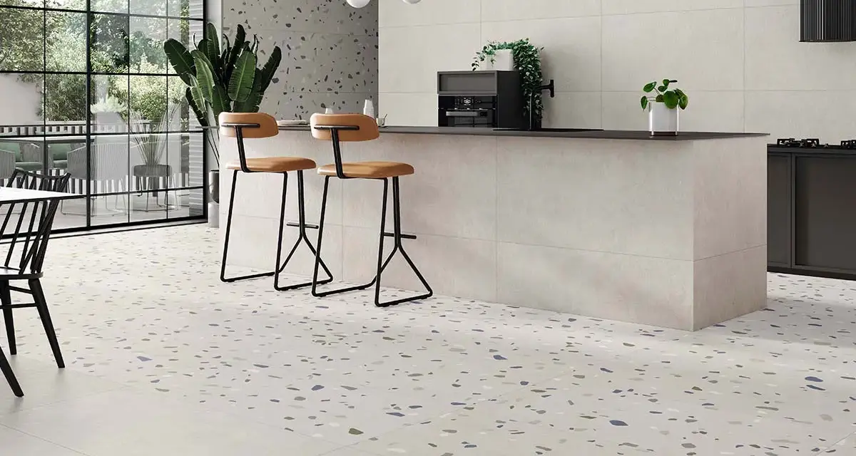 Suelos para cocinas blancas con diseño de terrazo moteado, isla central con taburetes y grandes ventanales.