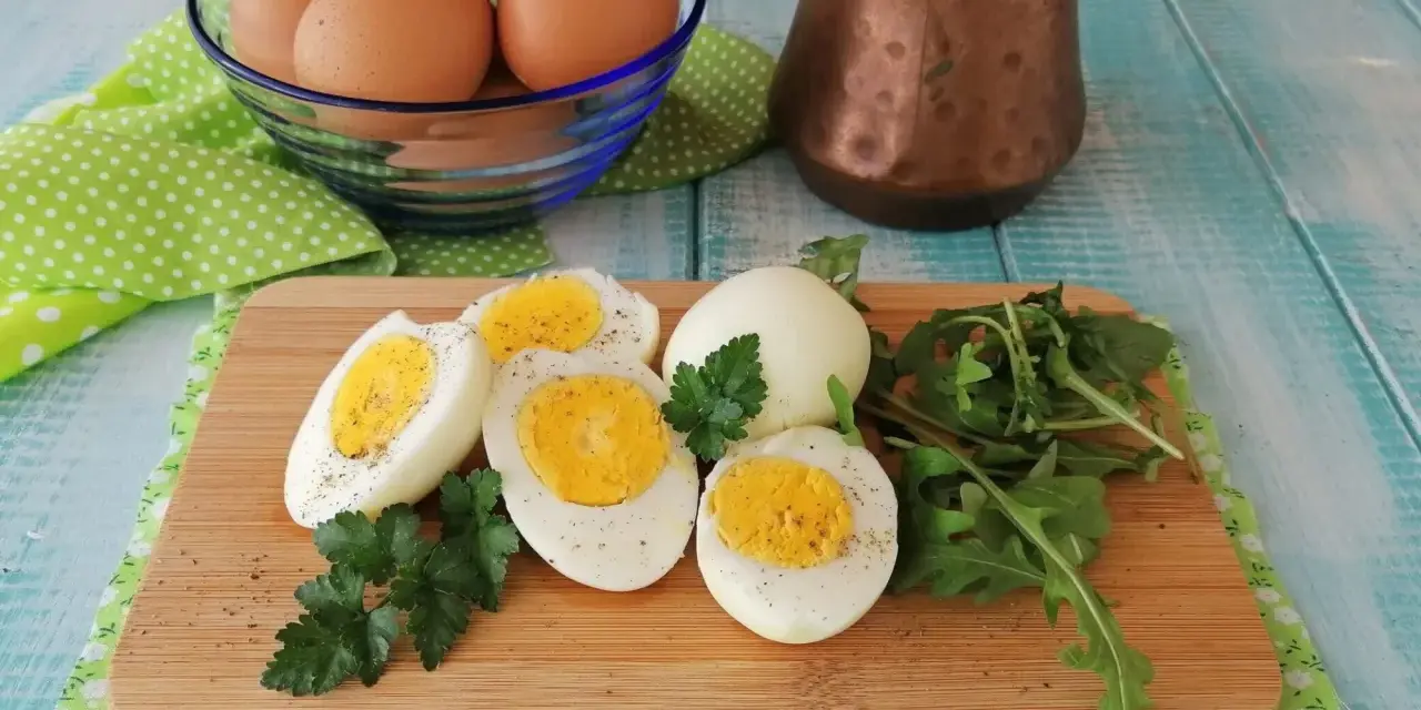 Uova sode in friggitrice ad aria, tagliate a metà, su tagliere con rucola e prezzemolo. Un modo sano e veloce per preparare le uova.