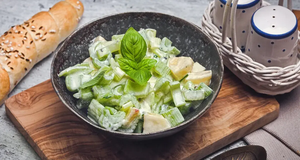 Ein cremiger sellerie salat mit frischem Basilikum, serviert in einer Schale neben einem Baguette und Salz- und Pfefferstreuern.