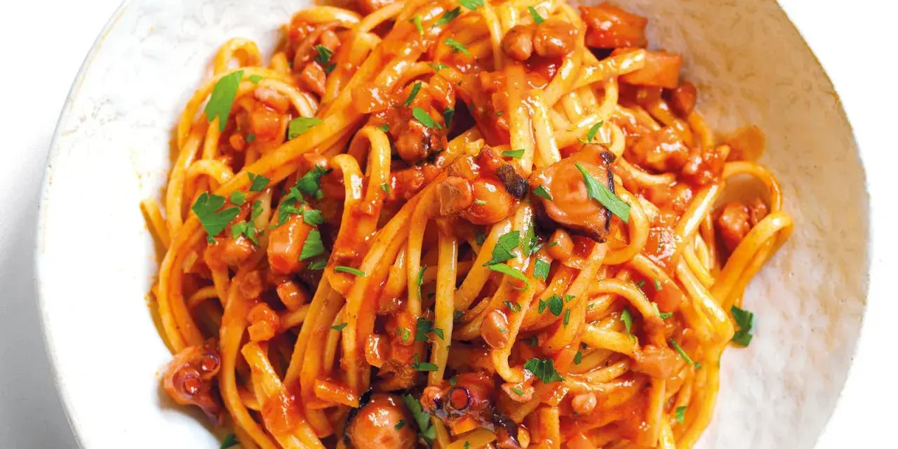 Linguine al ragù di pesce, un piatto saporito con polpo e pomodoro, guarnito con prezzemolo fresco.