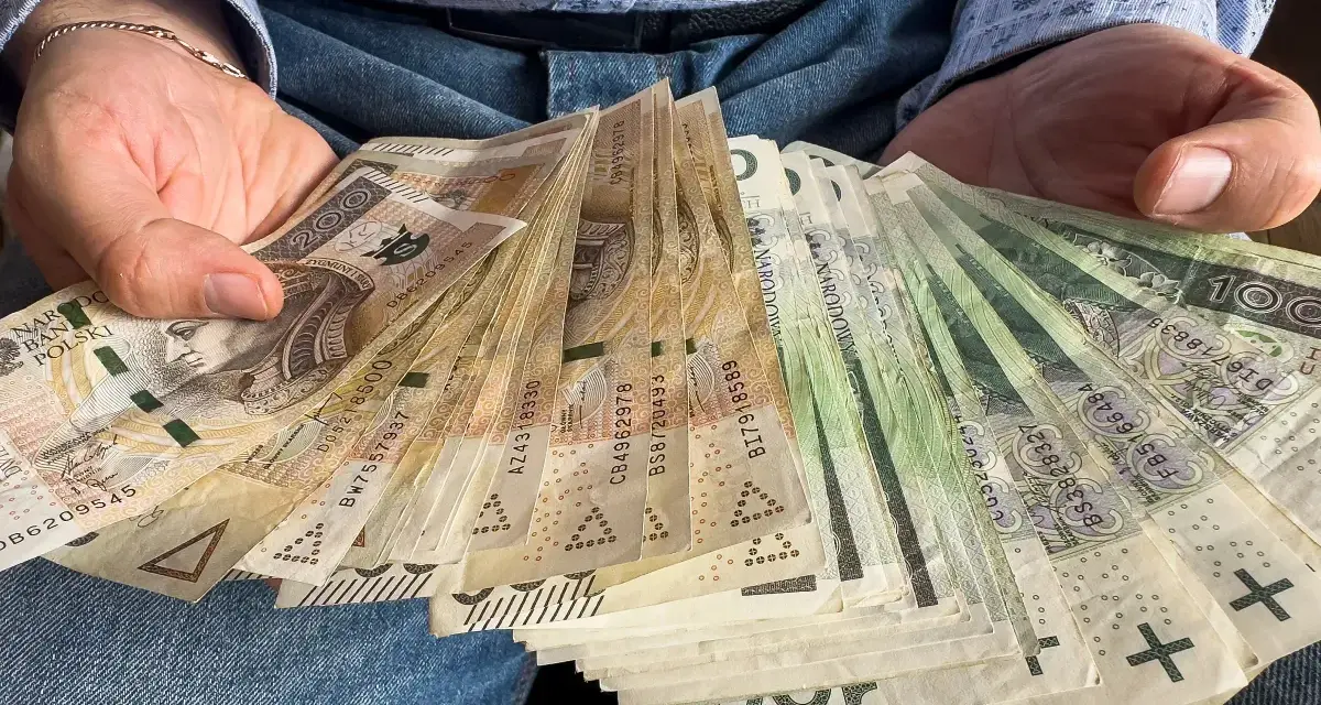 Ręce trzymające stos banknotów, w tym 1000 plus złotych. Widać portret Kopernika na jednym z banknotów.