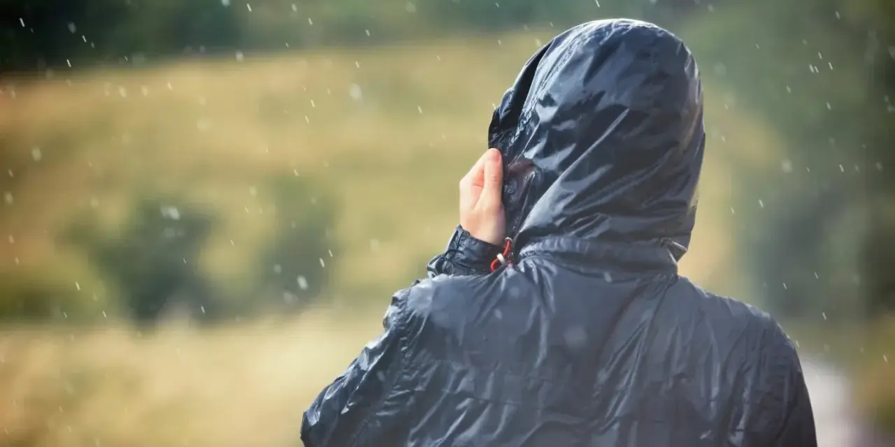 Person im Regen, die Kapuze einer Jacke mit PU-Beschichtung festhält.