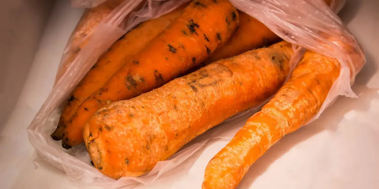Kilka pomarańczowych marchewek w plastikowej torbie, na których widać ciemne plamy, oznaki pleśni.