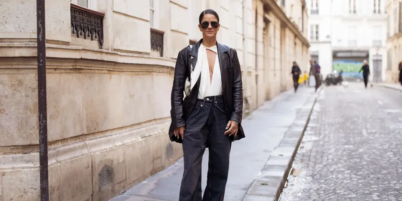 Mujer con gafas de sol y chaqueta de cuero, luciendo un elegante pantalón flare que es tendencia.