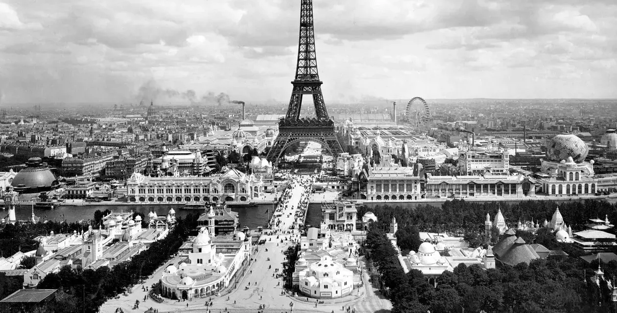 Vista panorámica del **Champ de Mars** con la Torre Eiffel dominando el paisaje, rodeada de pabellones y una noria.