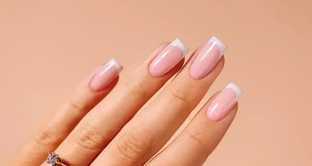 Dłonie z idealnym manicure french na paznokciach. Delikatny róż i biel tworzą klasyczny french na paznokciach, podkreślony subtelnym pierścionkiem.