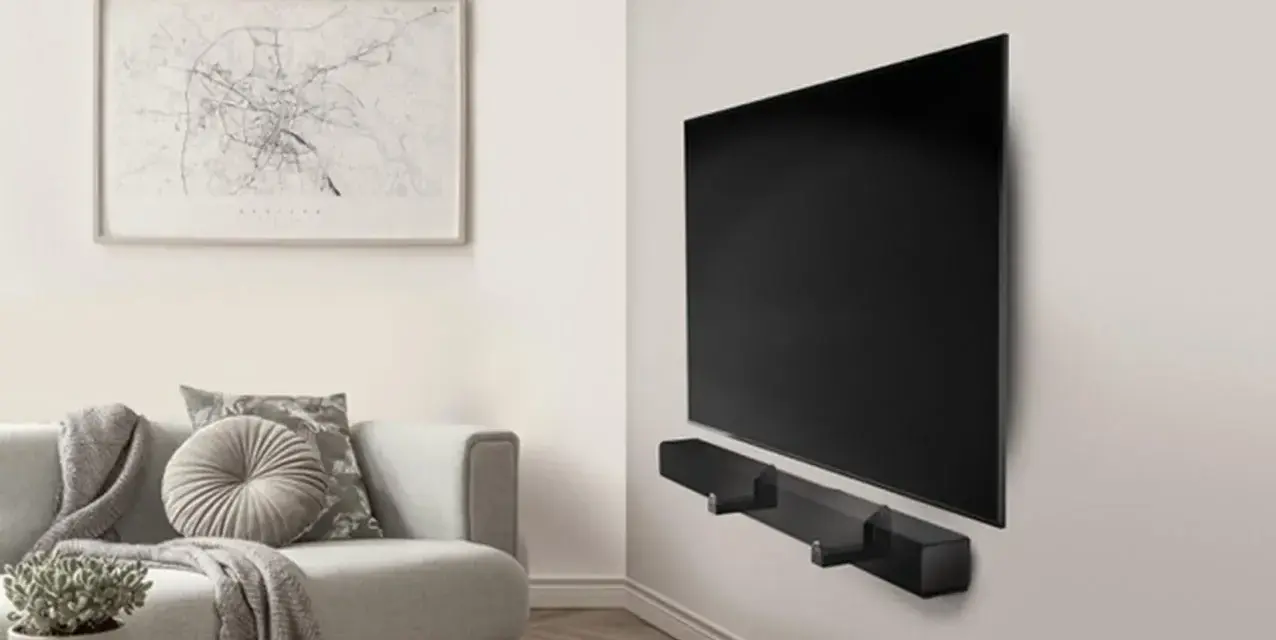 Un elegante soggiorno con un divano grigio e un quadro astratto. Al centro, un televisore a schermo piatto montato a parete con una soundbar nera.