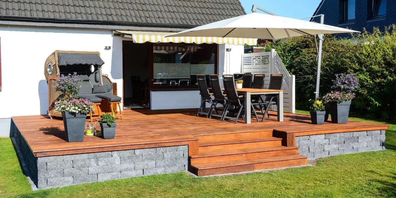 Eine 30 qm Terrasse gestalten: Holzdeck mit Sitzmöbeln, Esstisch, Sonnenschirm und Blumen. Perfekt für entspannte Stunden im Freien.