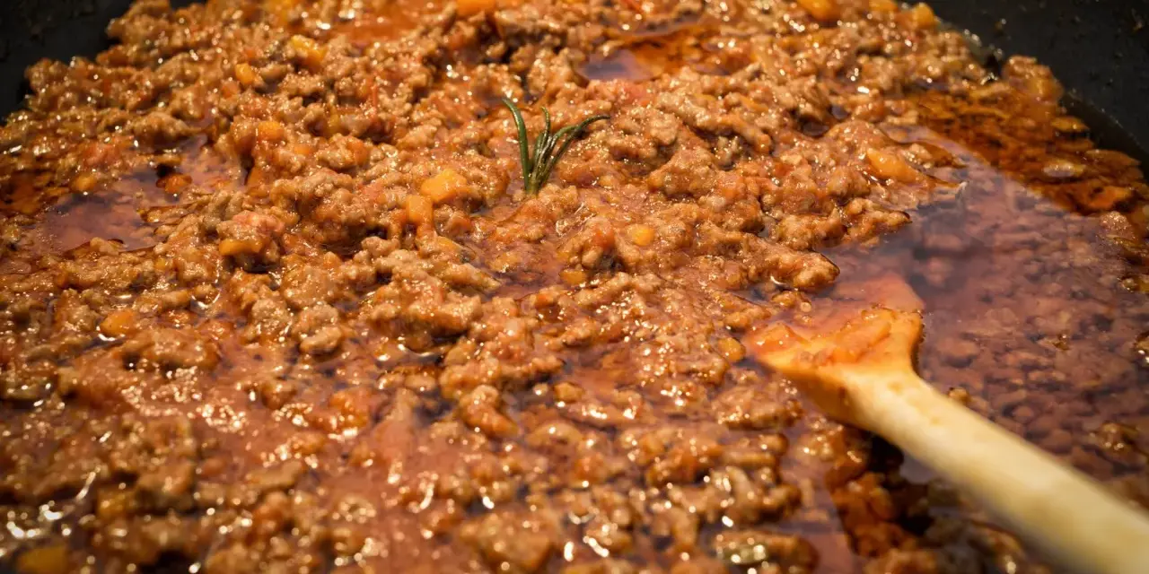 Un saporito ragù di lepre cuoce lentamente in padella, con un rametto di rosmarino che profuma l'aria.