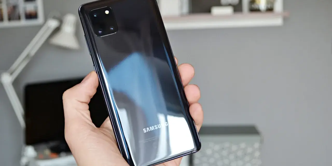 Dłoń trzyma błyszczący, czarny telefon Samsung A81 z modułem aparatów.