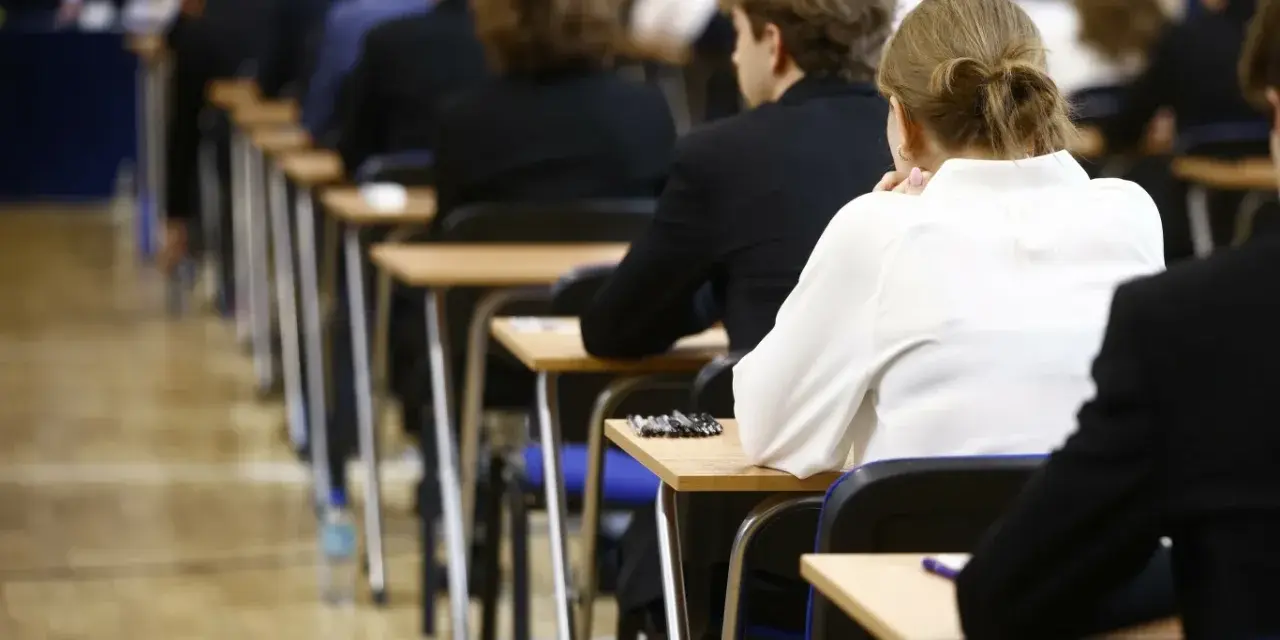 Uczniowie siedzą w rzędach przy ławkach, skupieni na rozwiązywaniu pytań maturalnych.