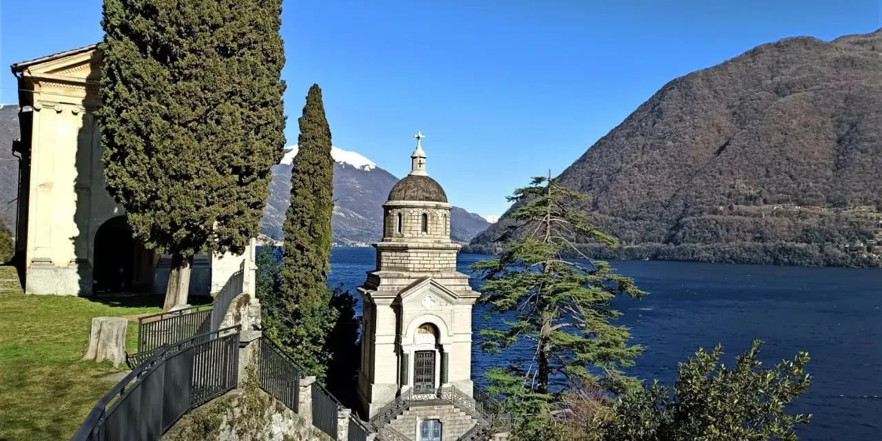 Un suggestivo lago con una piccola chiesa in mezzo, incorniciata da cipressi e montagne innevate.