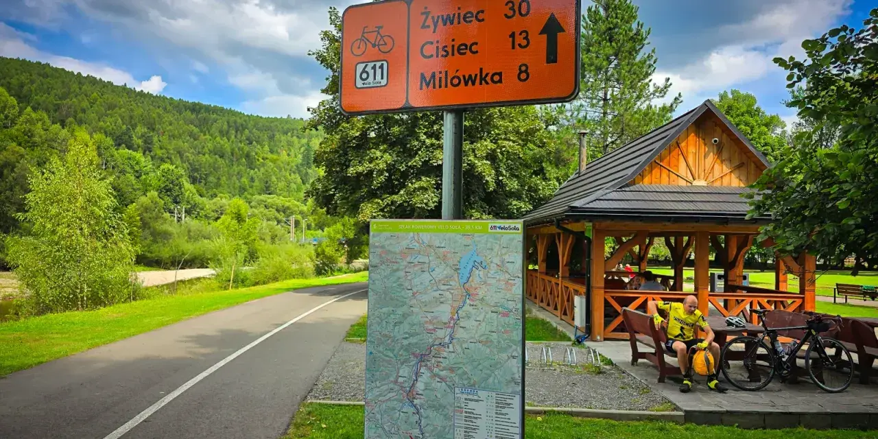 Znak drogowy dla rowerzystów na szlaku Velo Sola. Wskazuje kierunki i odległości do Żywca, Ciśca i Milówki. Obok mapa szlaku.