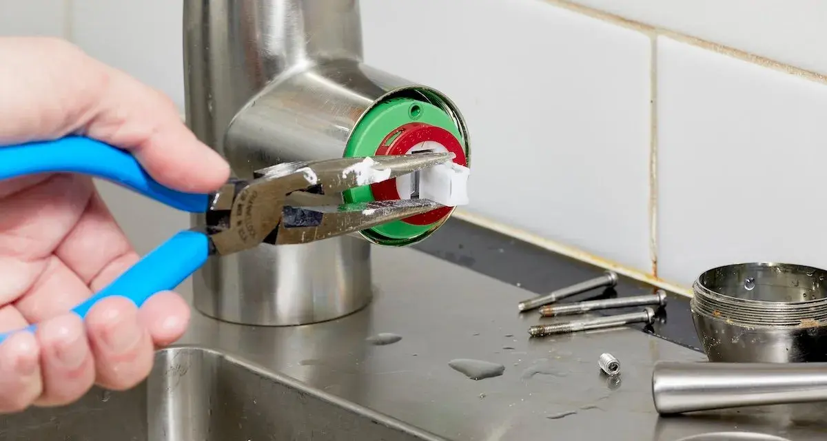A hand uses pliers to remove a faucet cartridge, a key step in learning how to replace faucet cartridge.