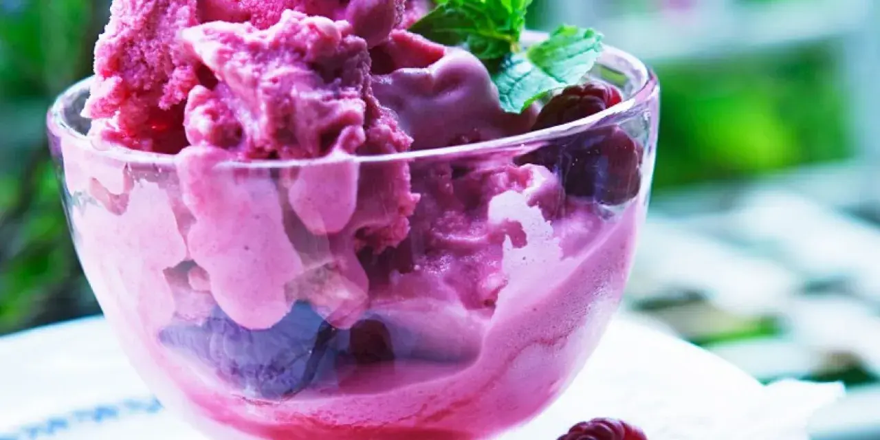 Himbeereis in einer Glasschale, frisch aus der Eismaschine, garniert mit Minze und ganzen Himbeeren.