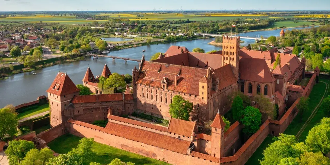 Malbork zamek krzyżacki, potężna twierdza z cegły, góruje nad rzeką Nogat. Otoczony murami, z wieżami i dziedzińcami, zaprasza do odkrywania historii.