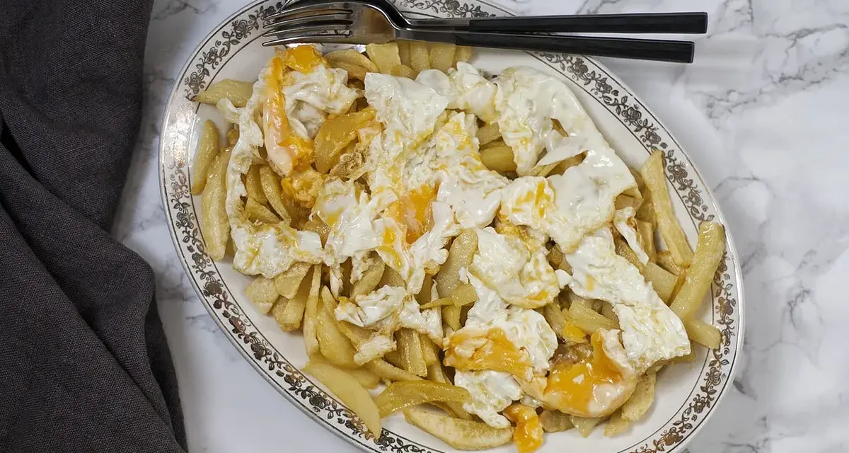 Plato de patatas fritas cubiertas con huevos rotos, con las yemas aún líquidas. Un clásico reconfortante.