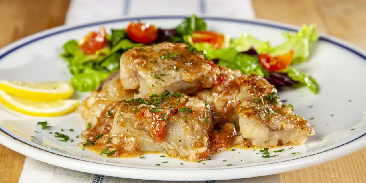 Deliziosa coda di rospo in umido con pomodoro e prezzemolo, servita con insalata fresca e spicchi di limone.