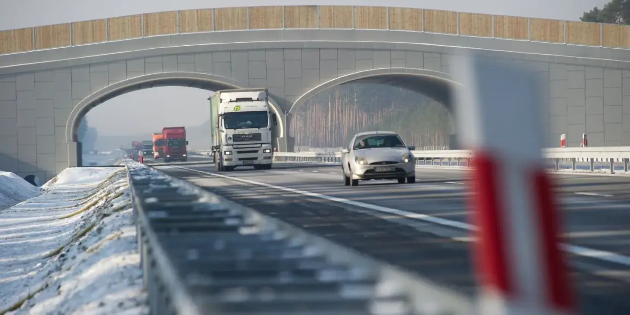Autostrada A2 z mostem nad jezdnią, jadące samochody i ciężarówki w zimowej scenerii.