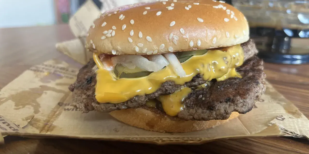 Podwójny cheeseburger z roztopionym serem, piklami i cebulą na bułce z sezamem.