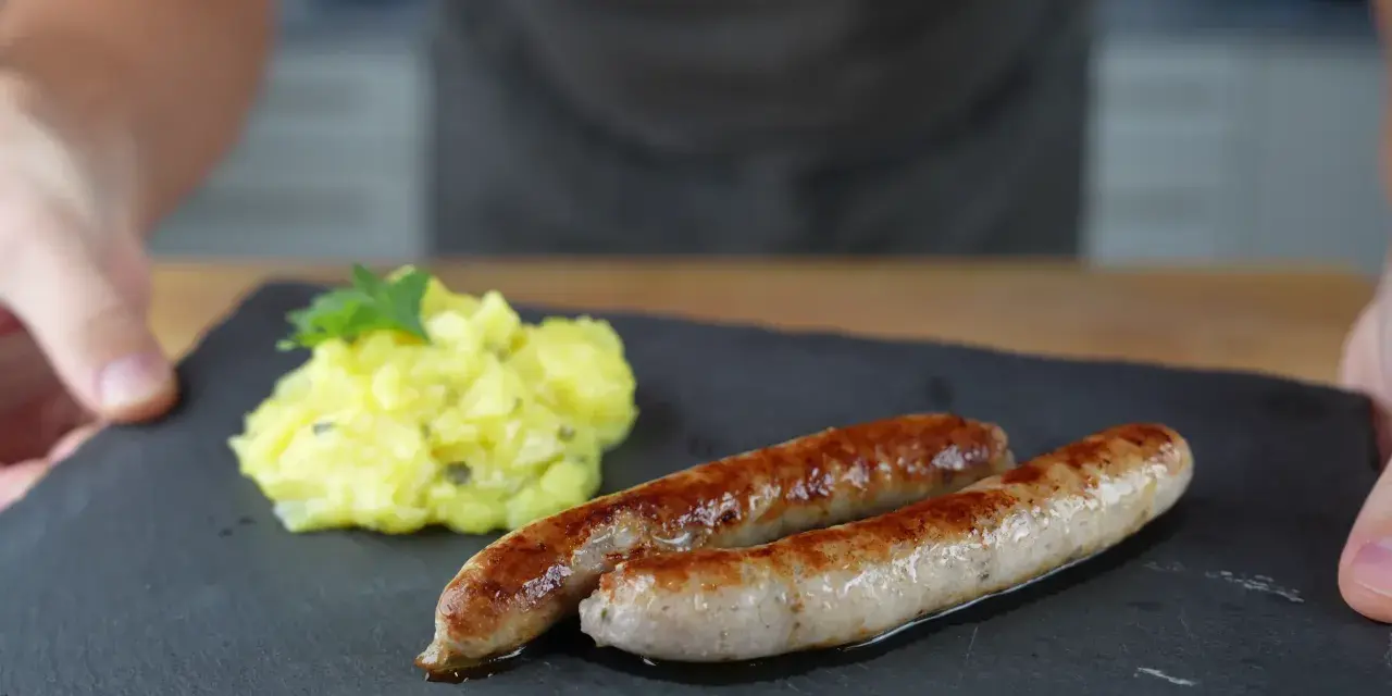 Zwei goldbraune Bratwürste mit Kartoffelsalat, perfekt für alle, die Bratwurst selber machen wollen.