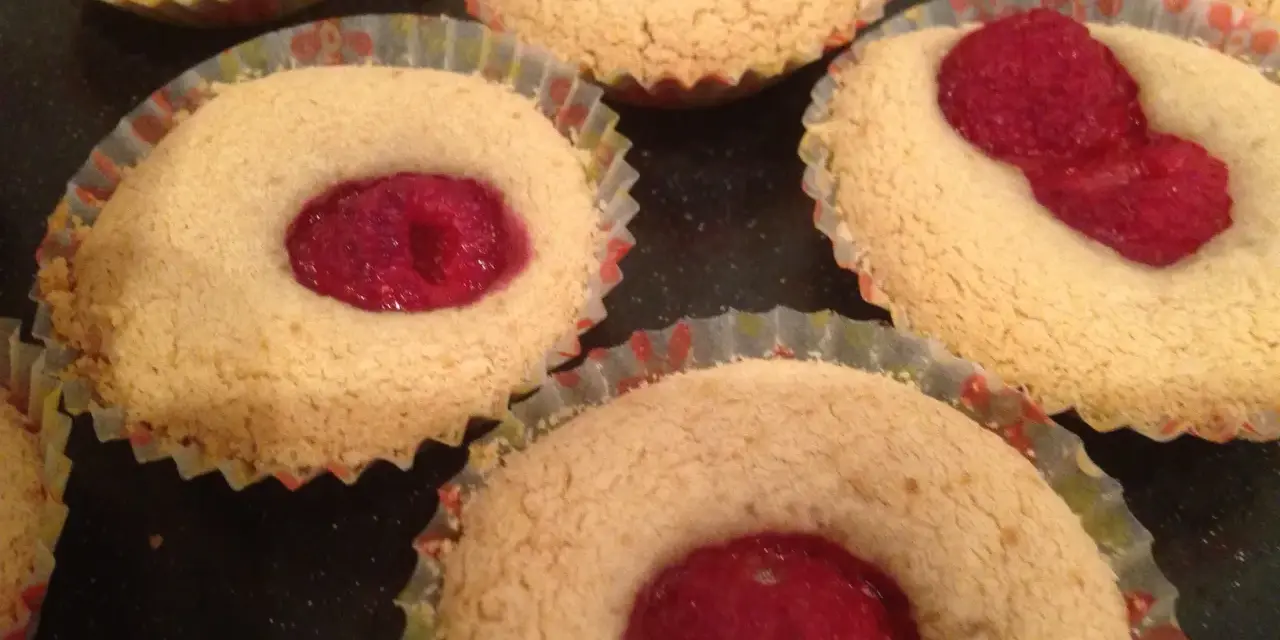 Flera glutenfria hallongrottor i pappersformar, med en hallon i mitten av varje.