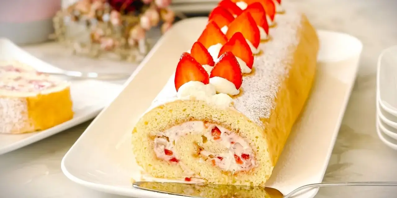 Ein köstliches Biskuitrolle Rezept mit frischen Erdbeeren und Sahne, bestäubt mit Puderzucker.