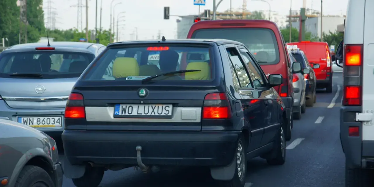 Czarny samochód z indywidualnymi tablicami rejestracyjnymi "WO LUXUS" w korku ulicznym.