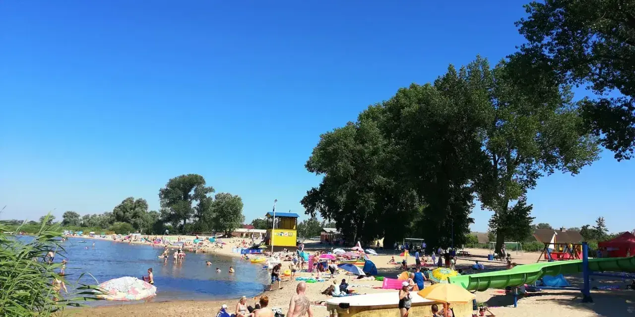 Słoneczny dzień na plaży, ludzie odpoczywają nad wodą. Zastanawiasz się, ile kilometrów jest ze Szczecina nad morze? To idealne miejsce na relaks przed podróżą.