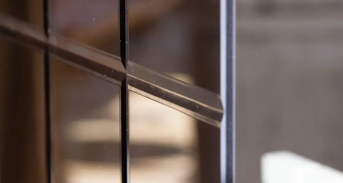 Dettaglio di un vetro con montanti scuri, riflessi tenui e polvere che si posa, creando un effetto quasi artistico.