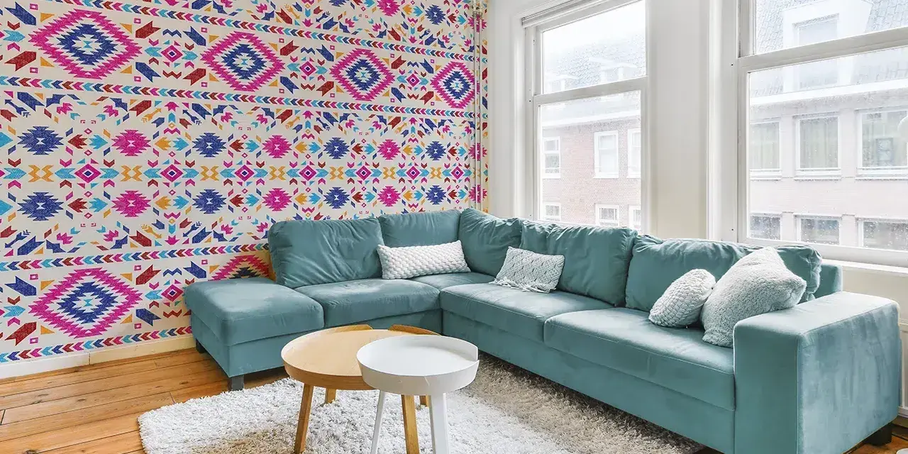 Un salon moderne avec un canapé bleu sarcelle et un papier peint intissé aux motifs ethniques colorés.