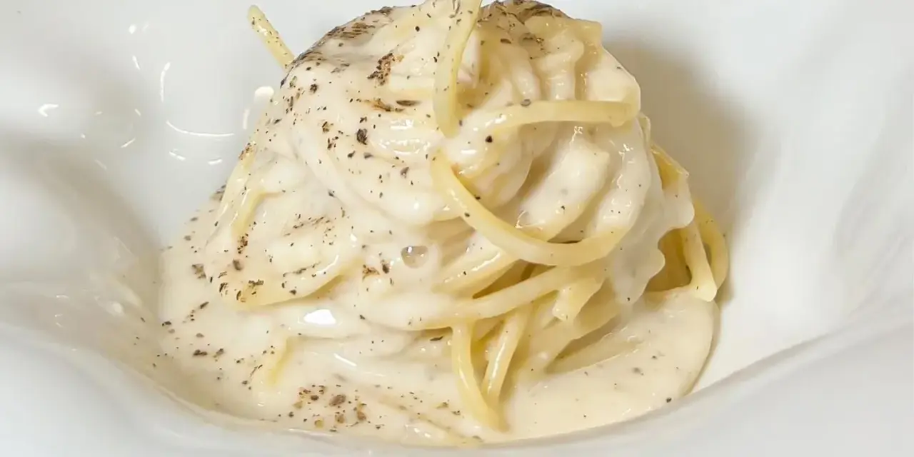 Un piatto di spaghetti cremosi, conditi con un'abbondante dose di cacio e pepe, cosparsi di pepe nero macinato.