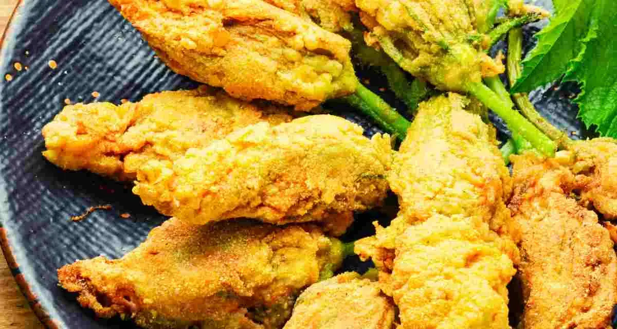 Fiori di zucca ripieni dorati e croccanti, serviti su un piatto blu scuro.