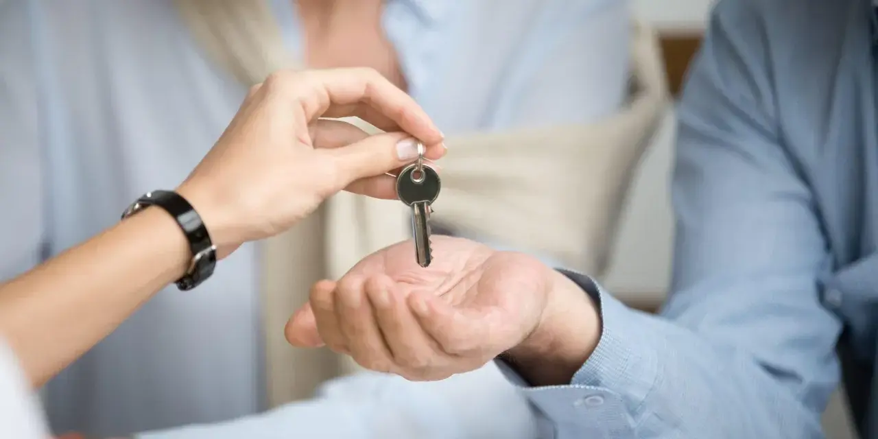 Una mano entrega una llave a otra, simbolizando el inicio de un nuevo hogar. Considera qué tener en cuenta al alquilar un piso.