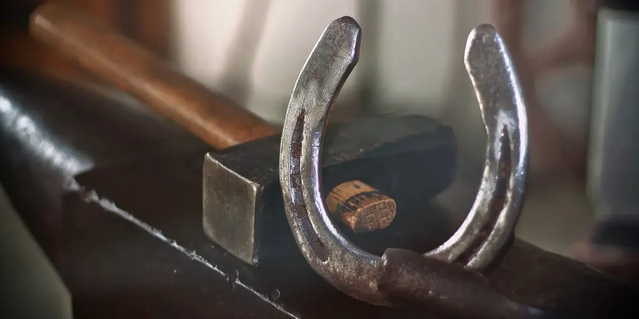 Un fer à cheval usé repose sur une enclume, à côté d'un marteau. L'artisanat du maréchal-ferrant est palpable.