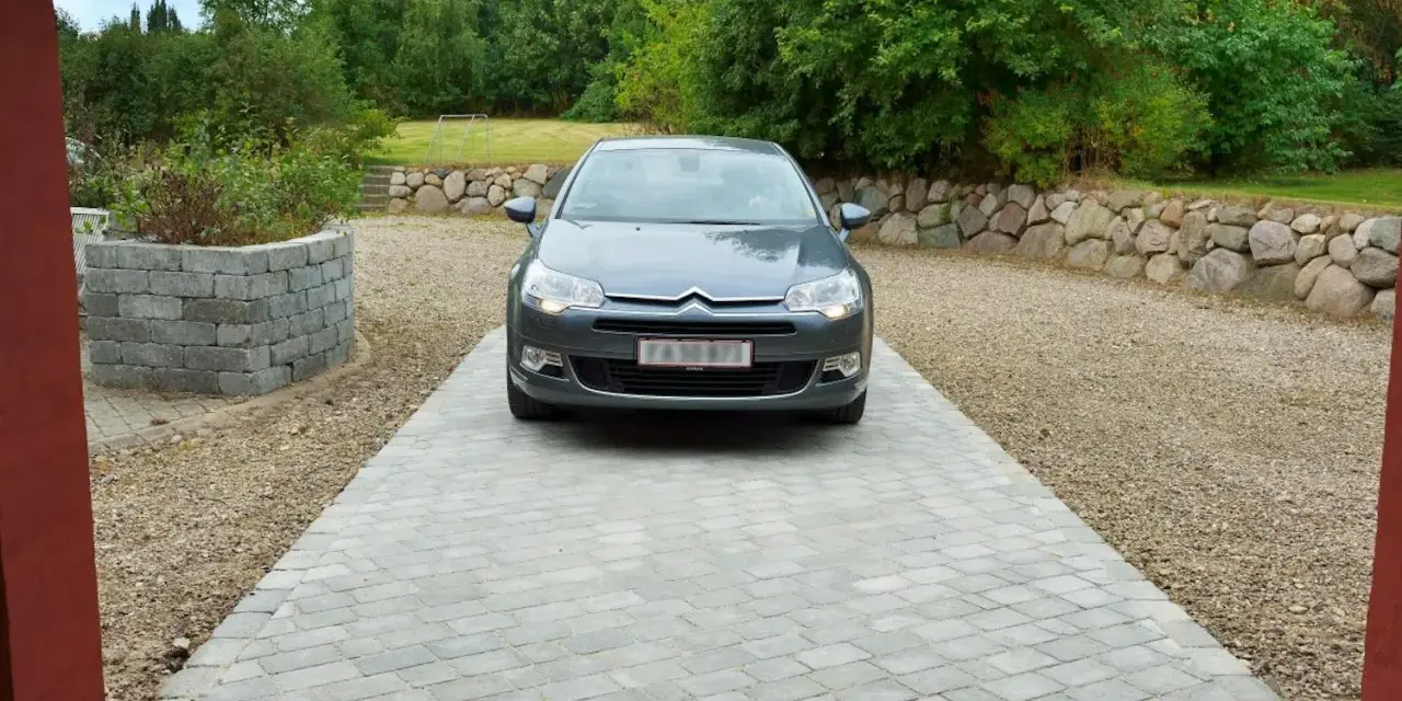 Grå bil parkerad på en vacker stenlagd uppfart. En fin uppfart inspiration med stenmur och grönska i bakgrunden.
