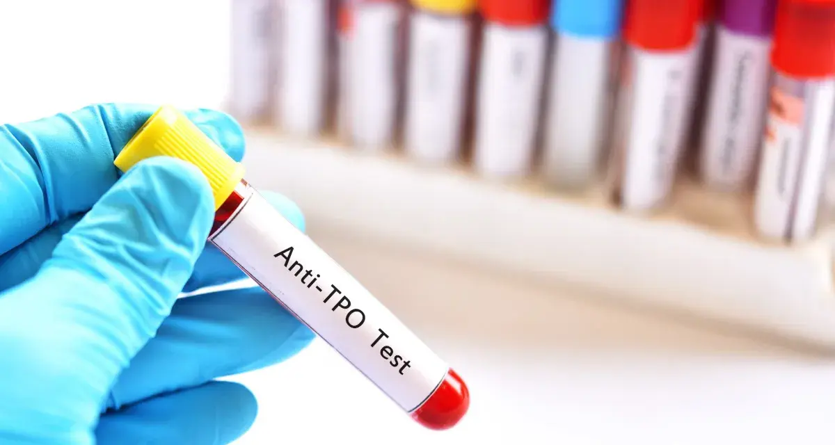 Ręka w niebieskiej rękawiczce trzyma probówkę z krwią do badań immunologicznych u dzieci. Test Anti-TPO.