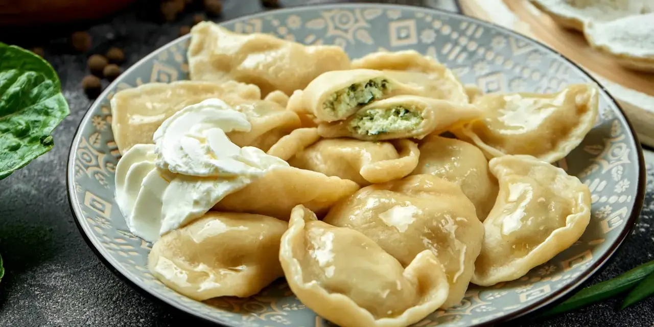 Talerz pierogów ze szpinakiem i twarogiem, z kleksem śmietany.