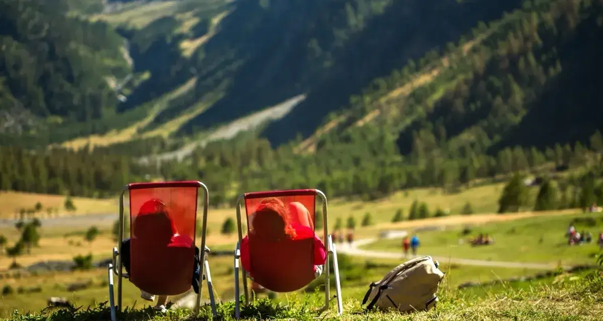 Dwie osoby w czerwonych leżakach podziwiają widok na Alpy w Austrii. Idealne miejsce na camping.