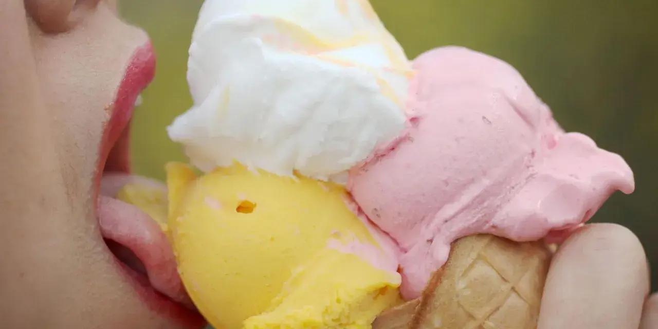 Eiscreme-Liebhaberin schleckt an einem Eis mit drei Kugeln. Die richtige guarkernmehl dosierung macht das Eis cremig.