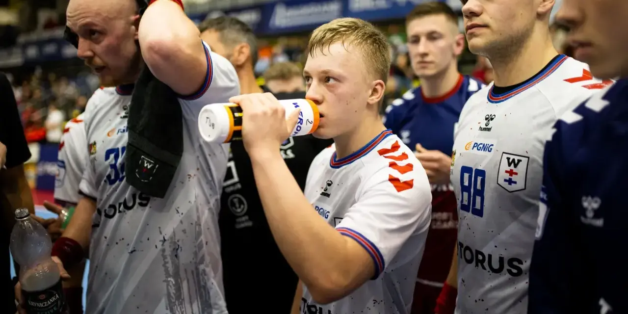 Szymon Adamczyk pije wodę z bidonu, otoczony kolegami z drużyny.