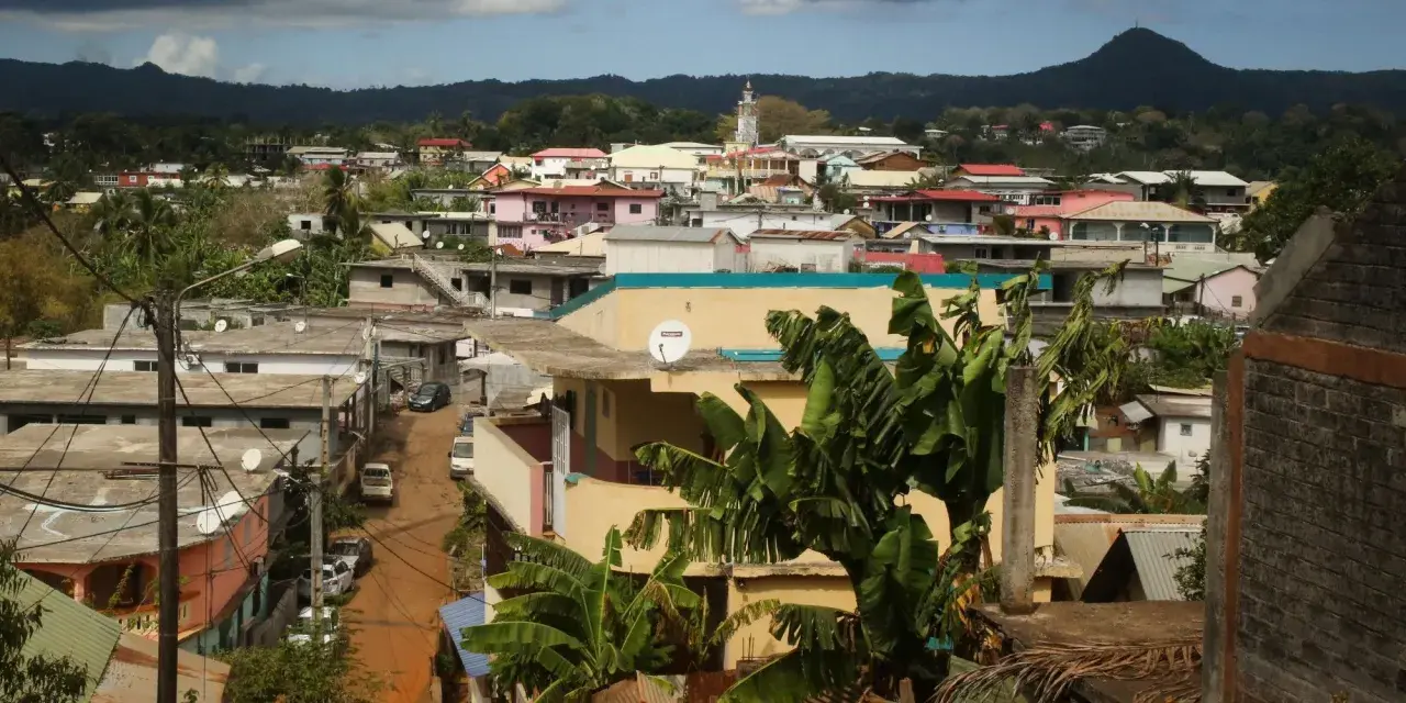 Vue d'une ville aux Comores, Mayotte, avec des maisons colorées, des bananiers et une montagne en arrière-plan.