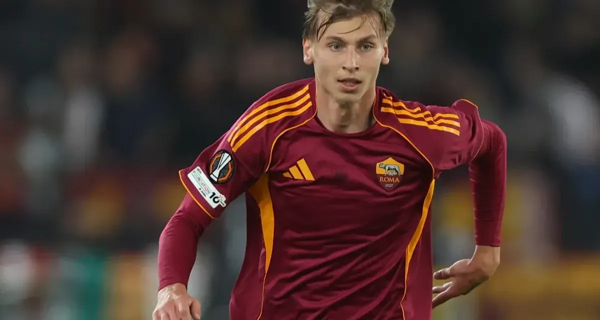 Piłkarz AS Roma w bordowej koszulce z żółtymi pasami, gotowy do gry przeciwko Genoa CFC.