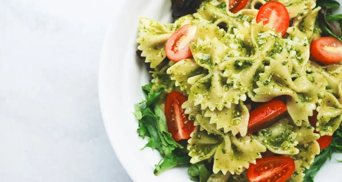 Pyszna sałatka z makaronem farfalle w sosie pesto, z pomidorkami koktajlowymi i świeżą sałatą.