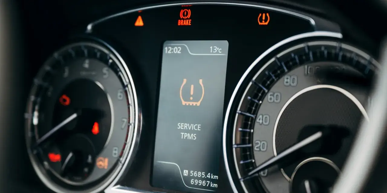 Na desce rozdzielczej świeci się kontrolka niskiego ciśnienia w oponach (TPMS). Obok widać wskaźnik hamulca i ostrzeżenie o temperaturze.