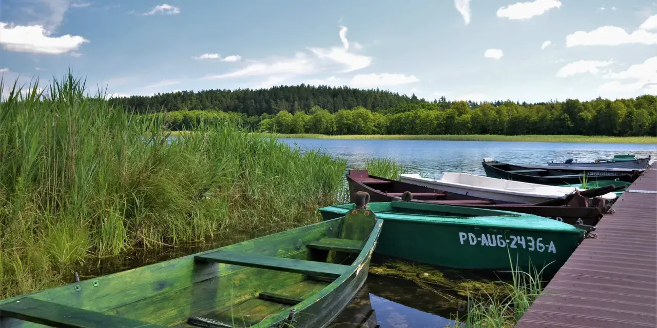 Zielone łodzie przy pomoście, idealne na wyprawę po jeziorach. Suwalszczyzna atrakcje czekają!