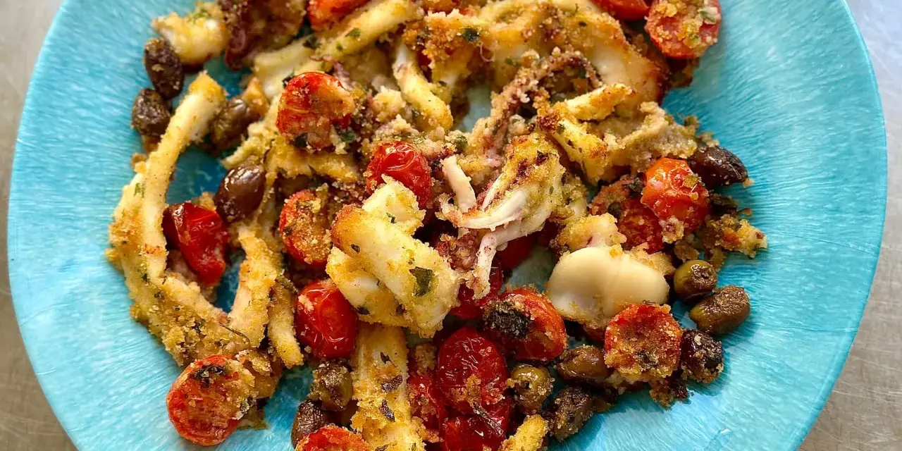 Calamari gratinati al forno su piatto blu, con pomodorini e olive.