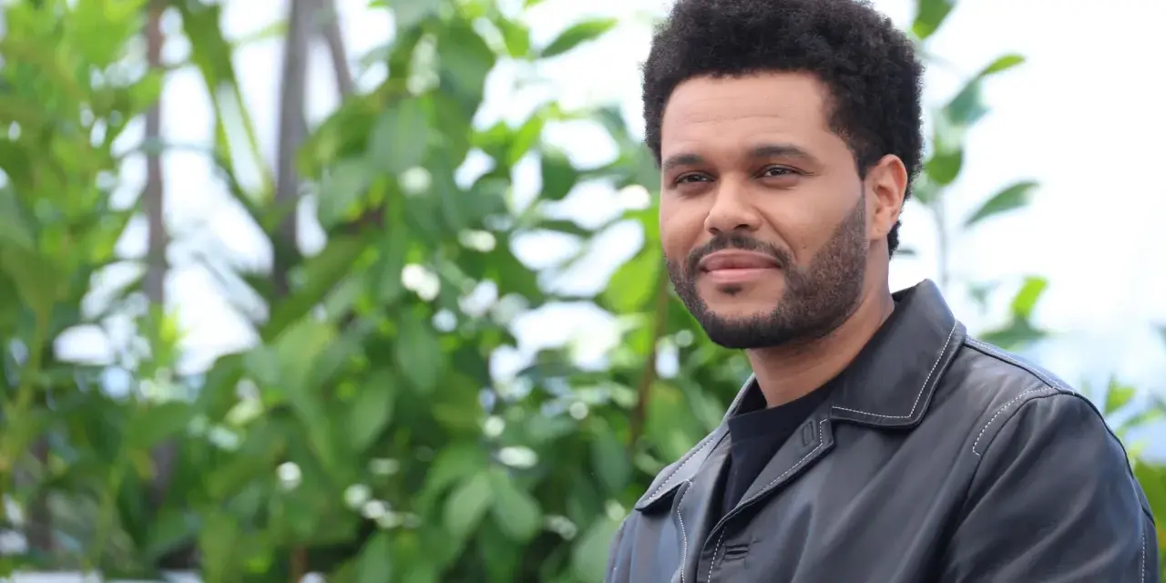The Weeknd trägt eine schwarze Lederjacke vor einem grünen, unscharfen Hintergrund.