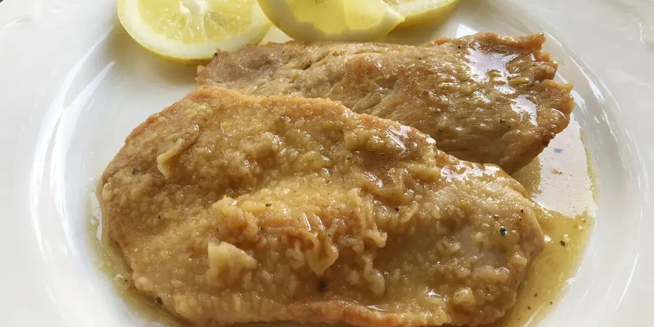 Deliziose scaloppine al limone, succulente e dorate, servite con spicchi di limone fresco.